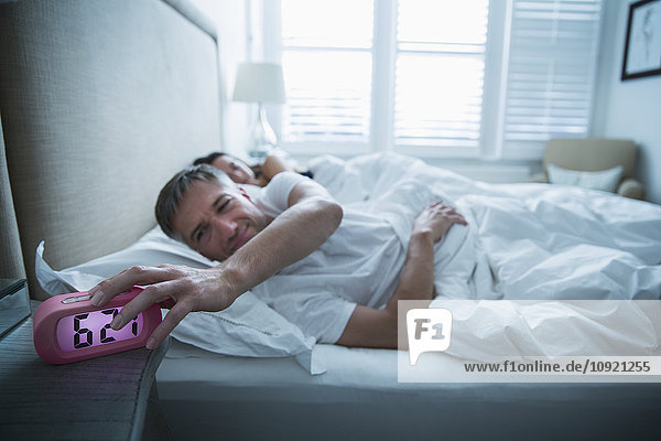 Man in bed turning off morning alarm clock