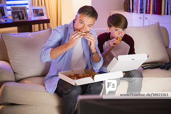 Father and son eating pizza and watching TV in living room