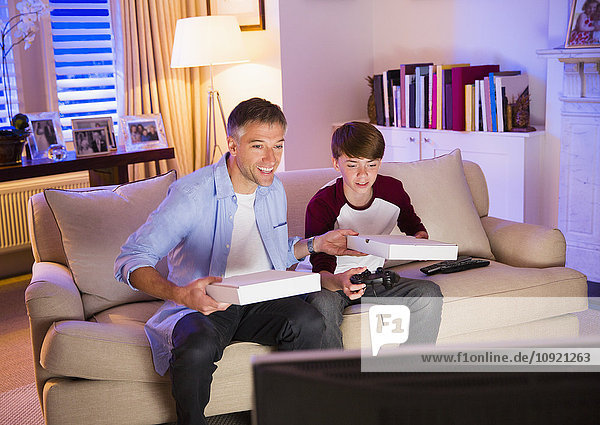 Vater und Sohn essen Pizza und spielen Videospiel im Wohnzimmer