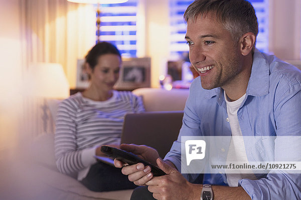 Ehefrau mit Laptop und Ehemann beim Fernsehen im Wohnzimmer