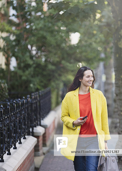 Lächelnde Frau geht mit dem Handy in den Stadtpark