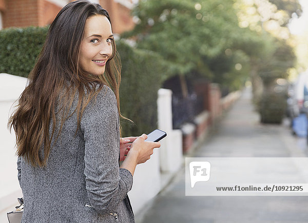 Portrait smiling businesswoman with cell phone looking back on sidewalk