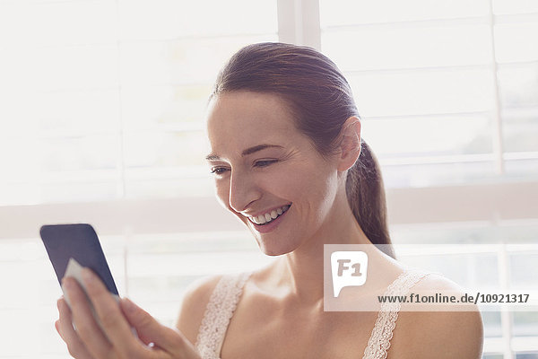 Lächelnde Frau SMS mit Handy am Fenster