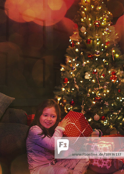 Neugieriges Mädchen schüttelt Geschenk am Weihnachtsbaum