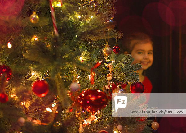 Portrait lächelndes Mädchen versteckt hinter dem Weihnachtsbaum