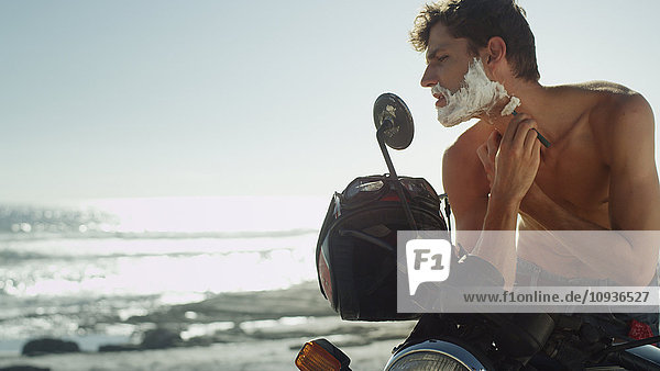 Junger Mann auf Motorrad rasiert Bart in der Nähe des Meeres