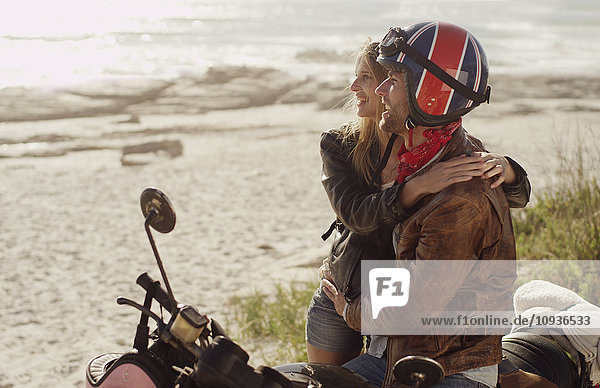 Junges Paar  das sich auf dem Motorrad umarmt und auf den Ozean blickt