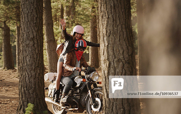 Übermütige junge Frau beim Motorradfahren im Wald