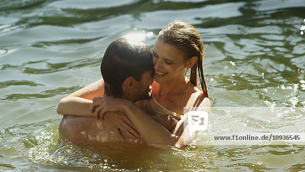 Zärtliches Paar,  das sich umarmt und im sonnigen See schwimmt