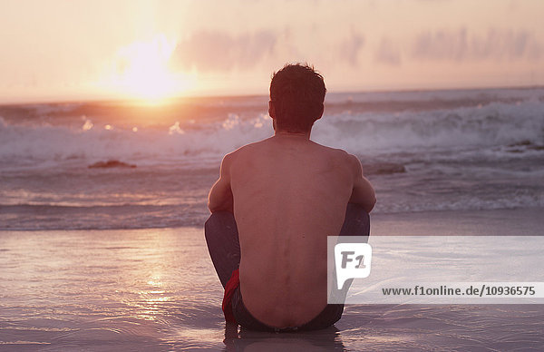 Nachdenklicher junger Mann am Strand bei Sonnenuntergang über dem Meer