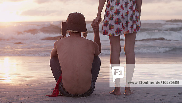 Junges Paar hält Hände am Strand bei Sonnenuntergang