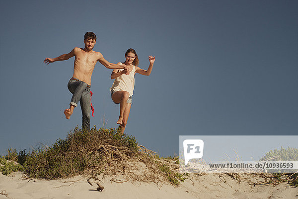 Verspieltes junges Paar springt am Sandstrand