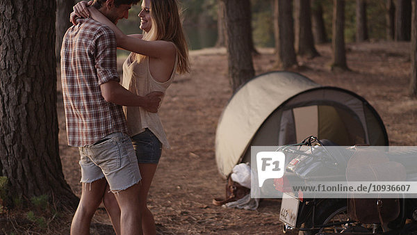 Zärtliches junges Paar  das sich vor einem Zelt im Wald umarmt