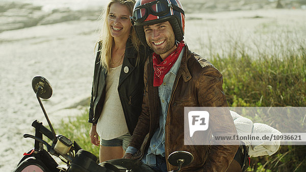Portrait lächelndes junges Paar auf Motorrad am Strand