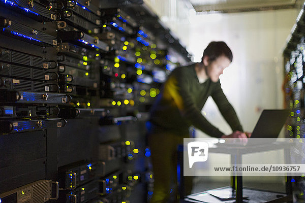Server room technician working at laptop in corridor