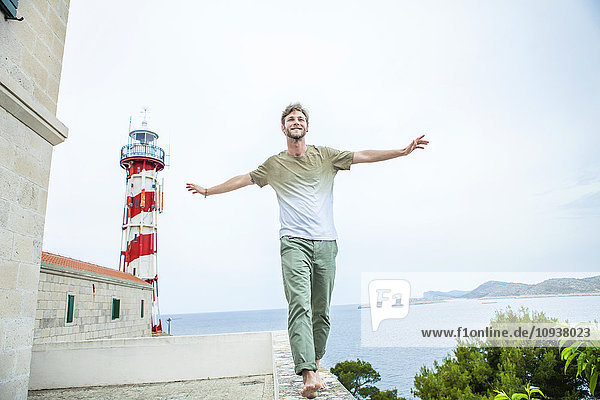 Young man balancing on wall with lighthouse in background