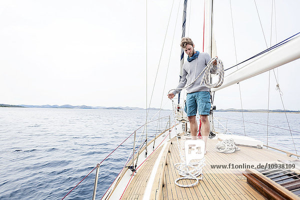 Young man on yacht curling up rope