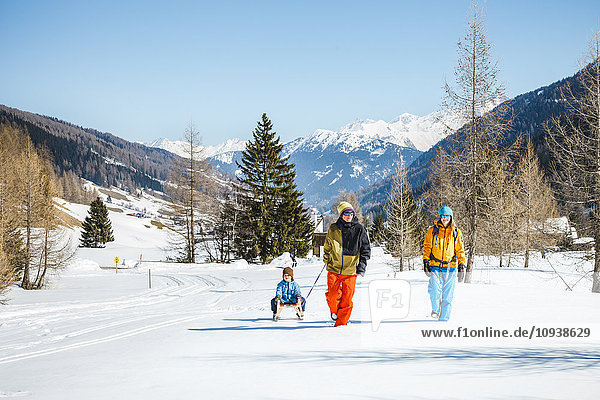 Family pulling sledge with son in Alpine winter scenery