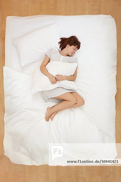 Frau liegt im Bett und hält Kissen