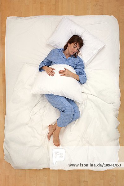 Frau liegt im Bett und hält Kissen