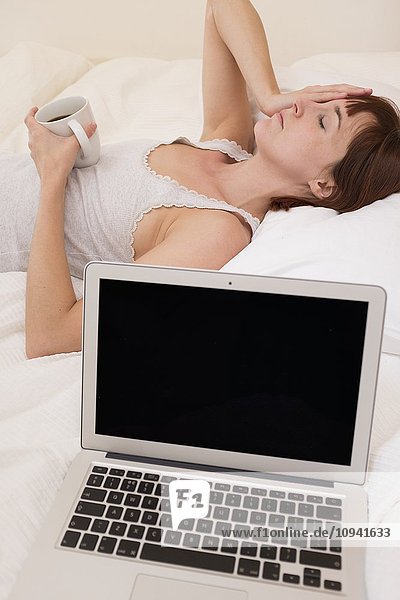 Erschöpfte Frau im Bett mit Laptop