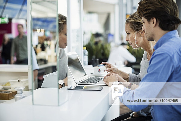 Seitenansicht der Geschäftsleute mit Kreditkarte und Laptop in der Flughafenlobby