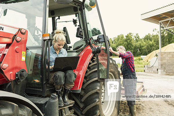 Frau benutzt Laptop während der Mann am Traktor steht.