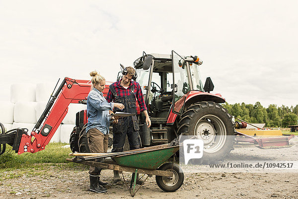 Frau zeigt den männlichen Arbeiter mit dem Traktor auf dem Bauernhof.