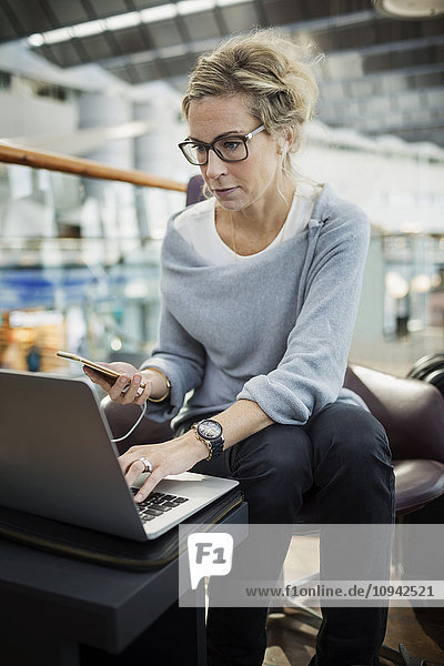 Geschäftsfrau mit Laptop und Smartphone in der Flughafen-Lobby