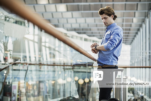 Side view of businessman checking the time while standing by glass railing at airport
