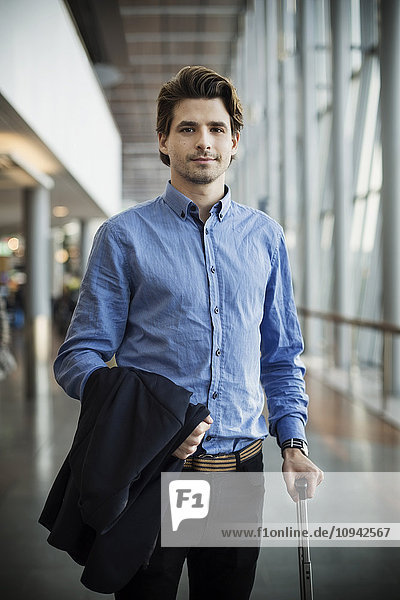 Portrait of confident businessman with luggage standing at airport