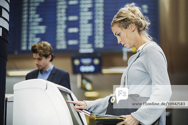 Seitenansicht der Geschäftsfrau mit Check-in-Maschine am Flughafen