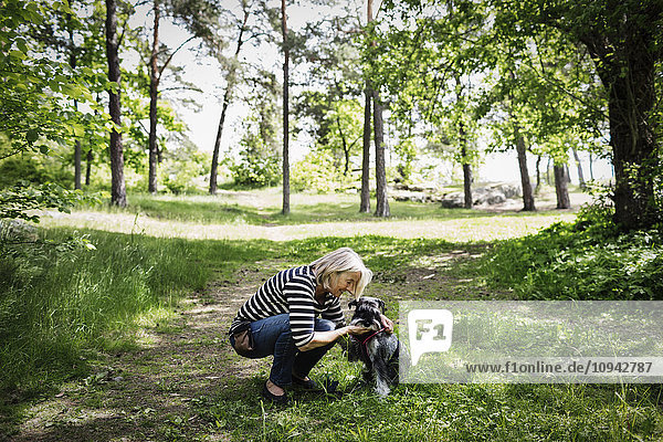 Side view of senior woman stroking dog while crouching on field