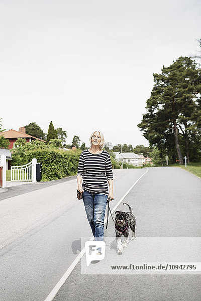 Volle Länge der älteren Frau  die mit Hund auf der Straße spazieren geht