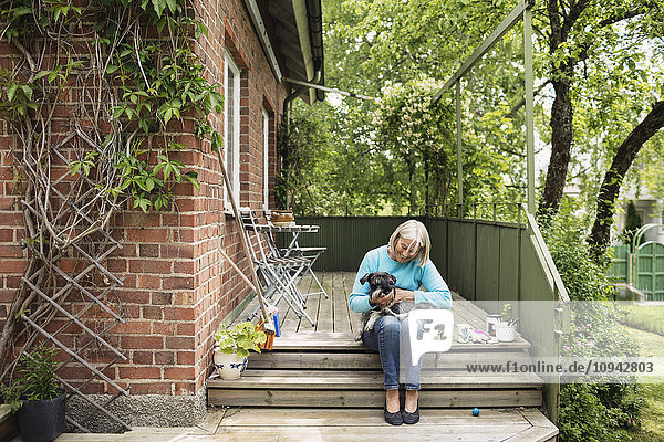 Glückliche Frau sitzend mit Hund auf Stufen vor dem Haus