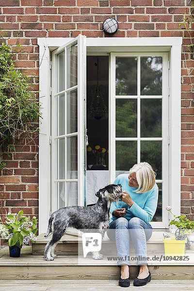 Glückliche Seniorin mit Hund am Hauseingang