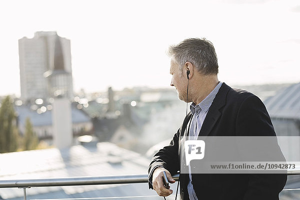 Businessman listening music and looking buildings while standing at office