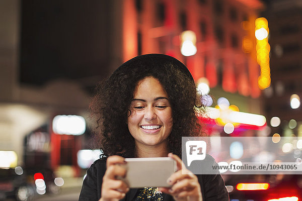 Happy young woman using smart phone in city at night