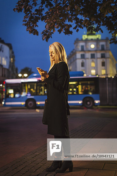 Volle Länge der Frau mit Smartphone in der Stadt Straße in der Nacht