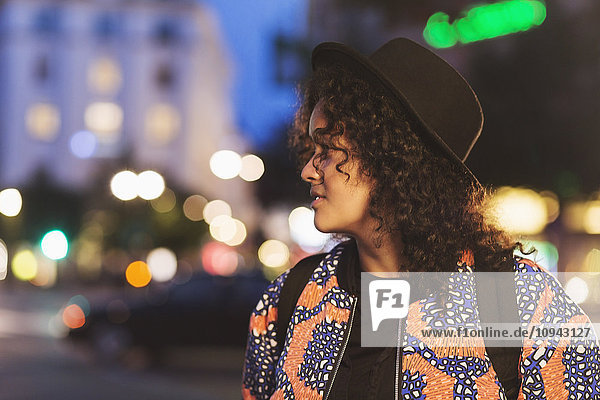 Woman looking away while standing on city street at night