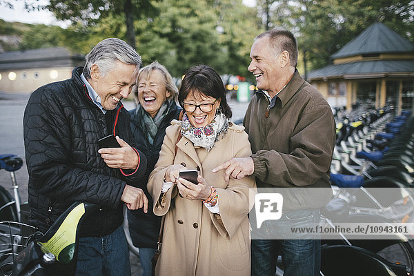 Glückliche Seniorenpaare mit Mobiltelefonen am Fahrradparkplatz