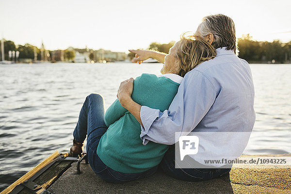 Senior man showing something to woman while sitting on pier