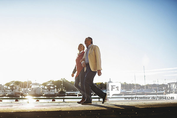 Full length of loving senior couple walking on pier against sky