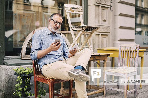 Man using mobile phone while sitting on chair outside antique shop