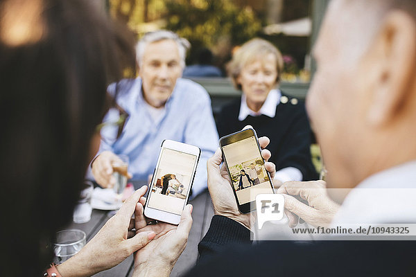 Seniorenpaar beim Betrachten von Fotos auf dem Handy im Außenrestaurant