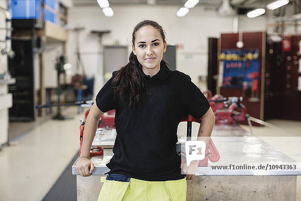 Portrait of smiling female auto mechanic student standing in workshop