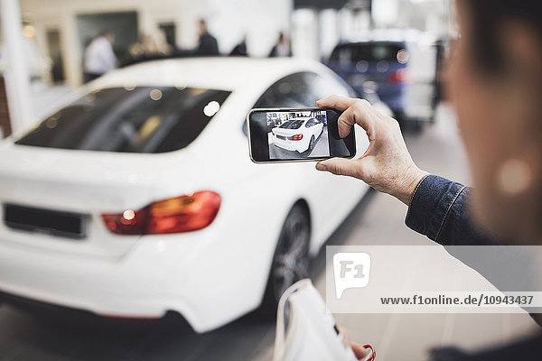 Senior woman photographing new car through mobile phone at showroom