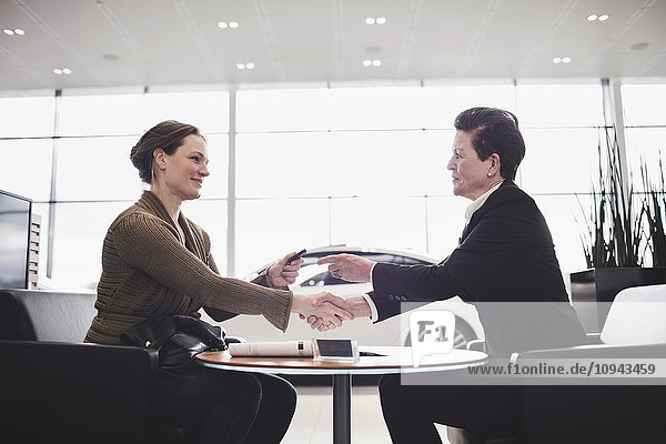 Saleswoman and customer shaking hands while talking at desk in showroom