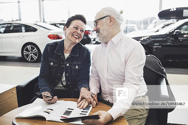 Fröhliches Seniorenpaar liest Broschüre im Autohaus