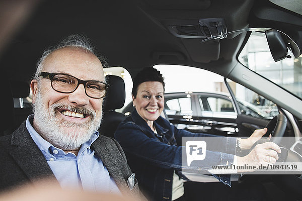 Portrait of happy senior man and woman sitting in car at showroom